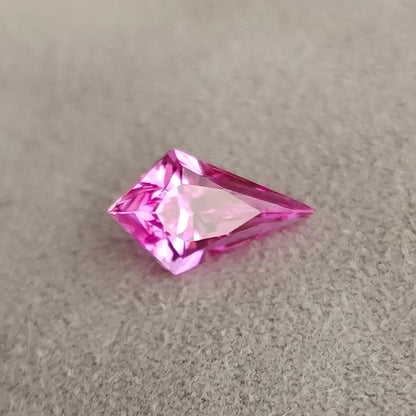 Angled view of a vivid pink kite cut gem lying on grey fabric, showing pavilion reflections.