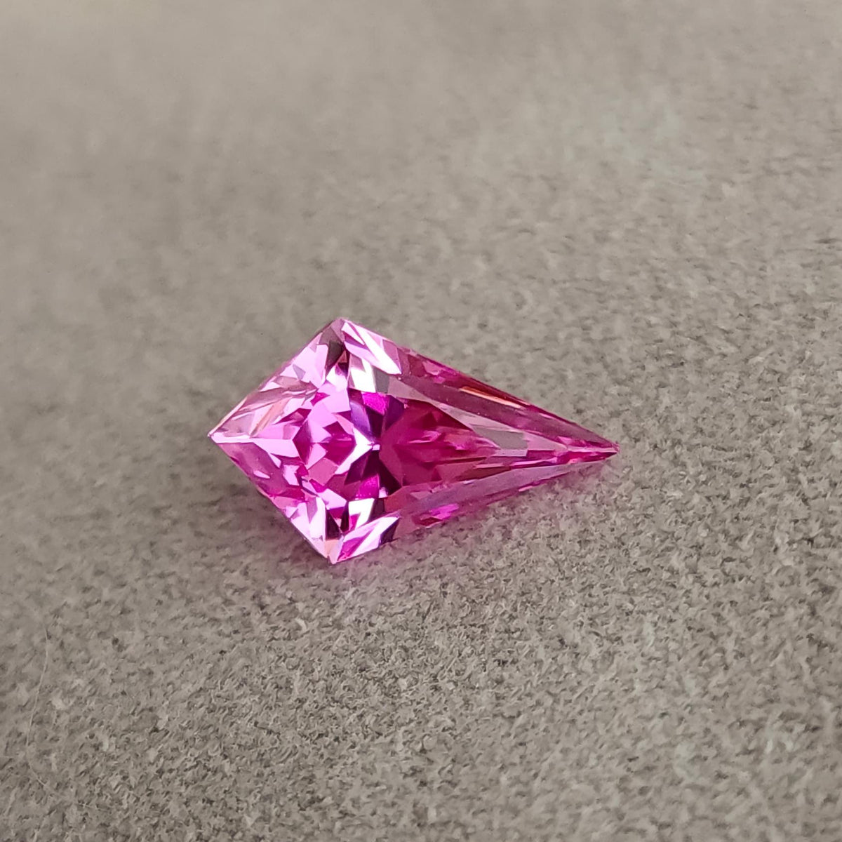 Low-angle side view of a faceted kite cut pink gemstone resting on fabric, showing facet geometry and profile.