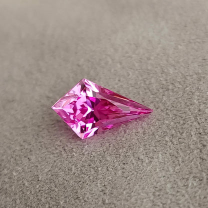 Low-angle side view of a faceted kite cut pink gemstone resting on fabric, showing facet geometry and profile.