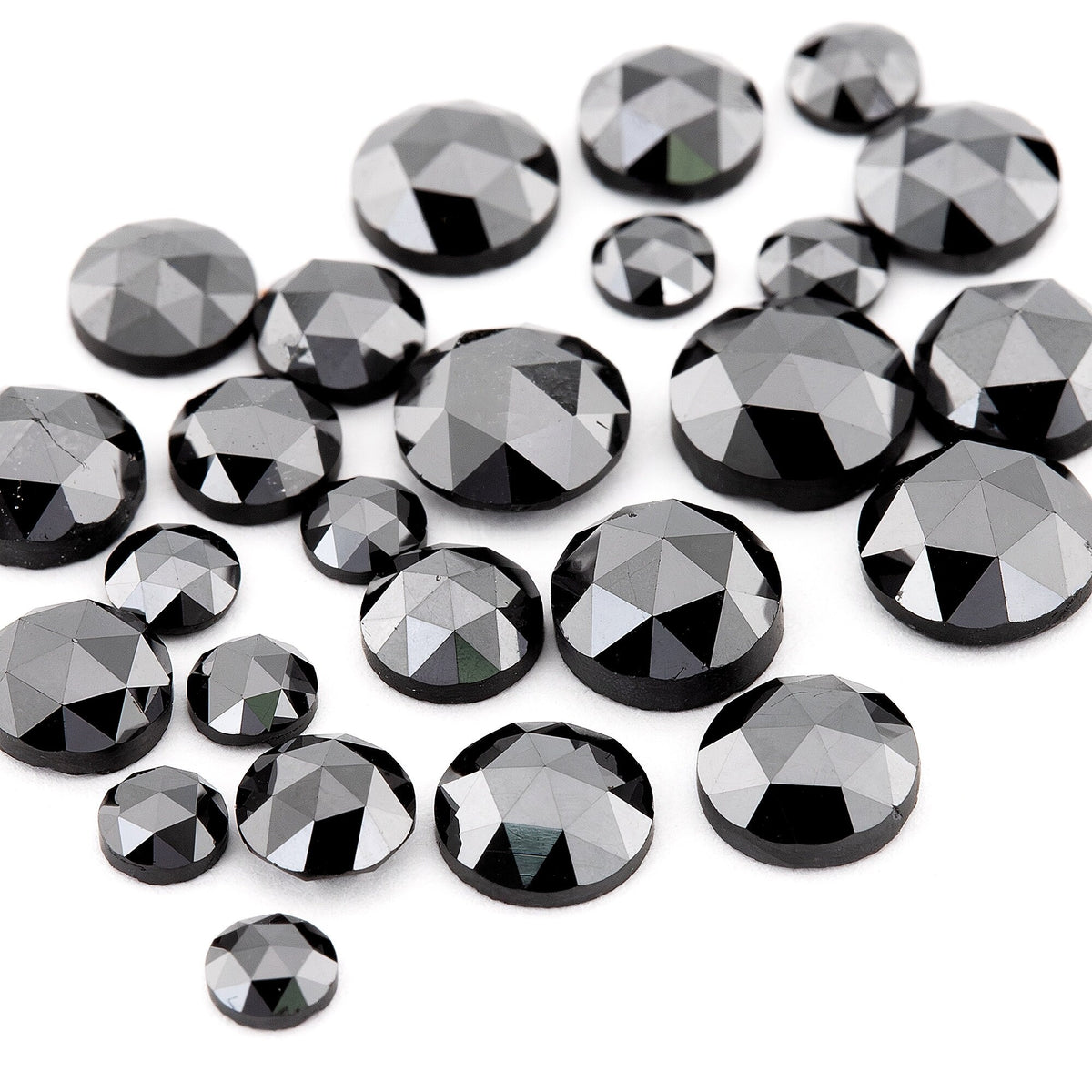 Close oblique view of black rose-cut diamonds on white, revealing low crowns, varied diameters and reflective triangular facets.