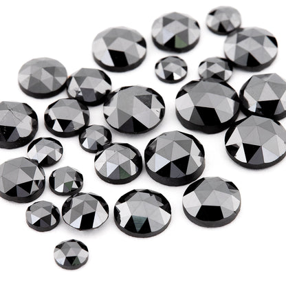 Close oblique view of black rose-cut diamonds on white, revealing low crowns, varied diameters and reflective triangular facets.