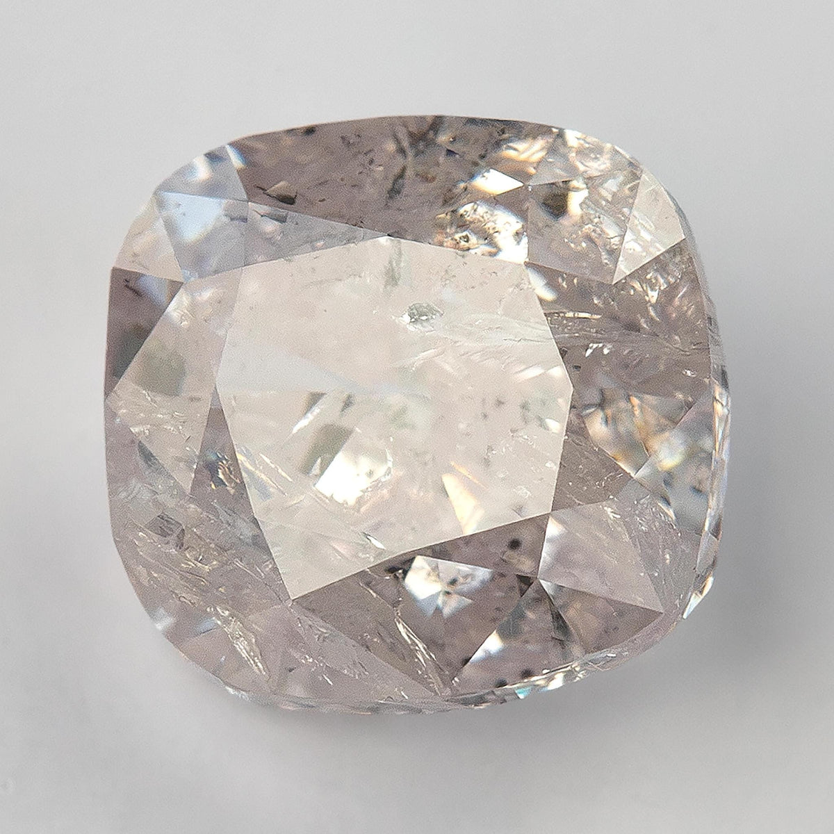 Natural light pink cushion diamond tilted under light, showing a bright central reflection and included interior.