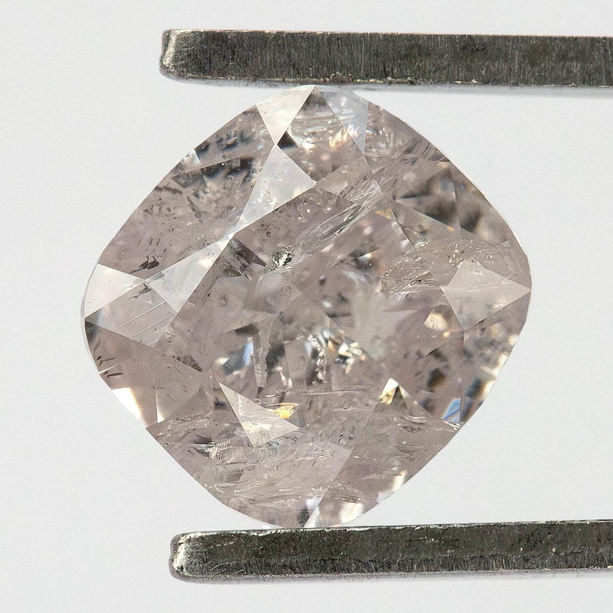 Natural light pink cushion diamond held face-up in tweezers, showing its outline and heavy inclusions.