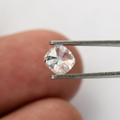 Rear view of the natural cushion diamond held in tweezers beside a fingertip for relative size.