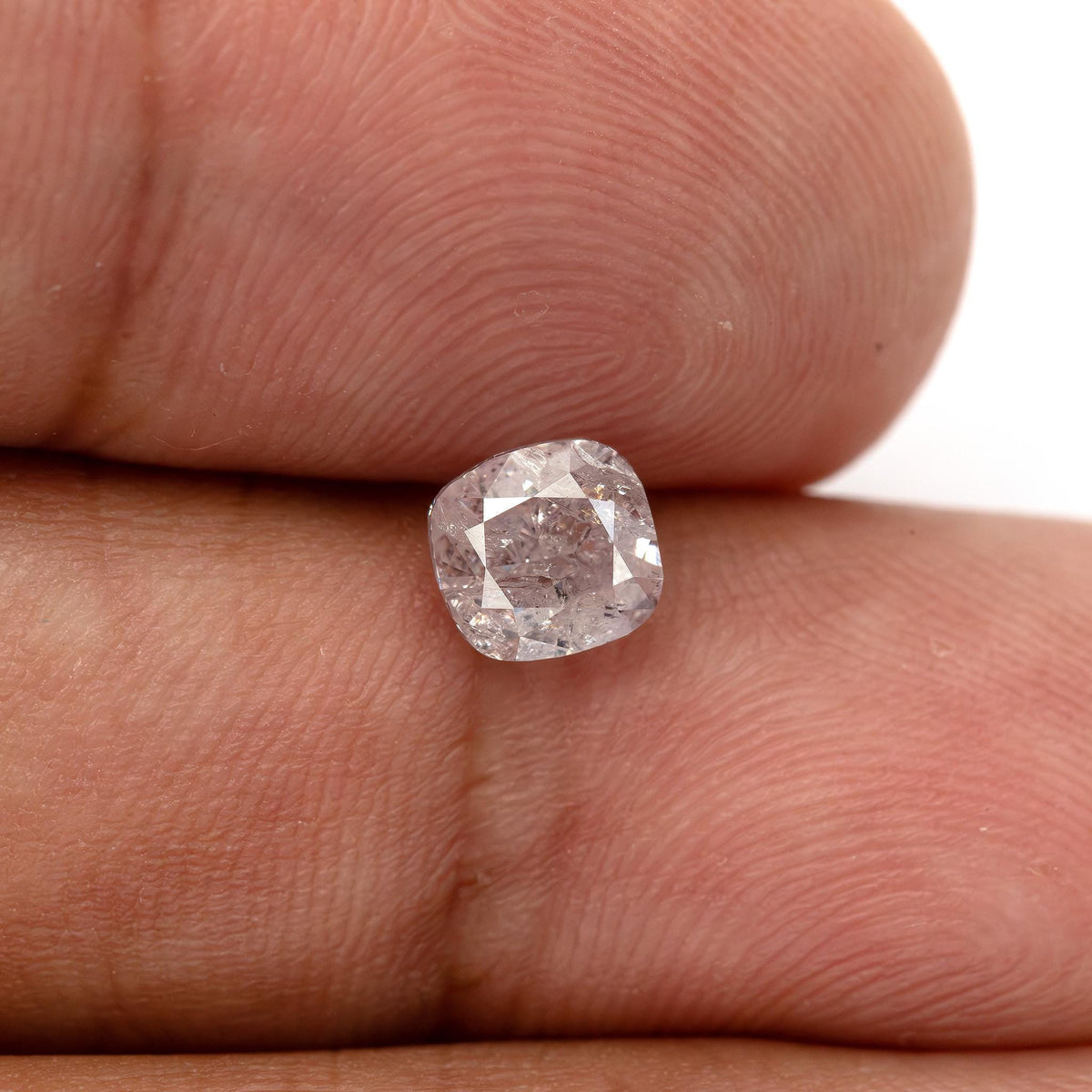 Natural light pink cushion diamond resting on fingertips, showing its face-up size and soft pink appearance.