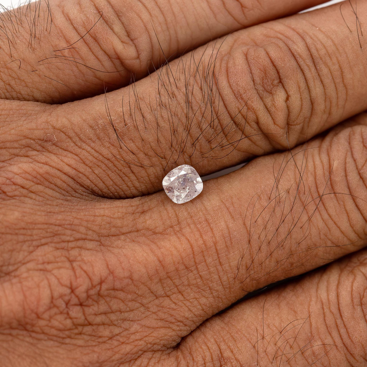 Loose light pink cushion diamond resting on the back of a hand for relative size.