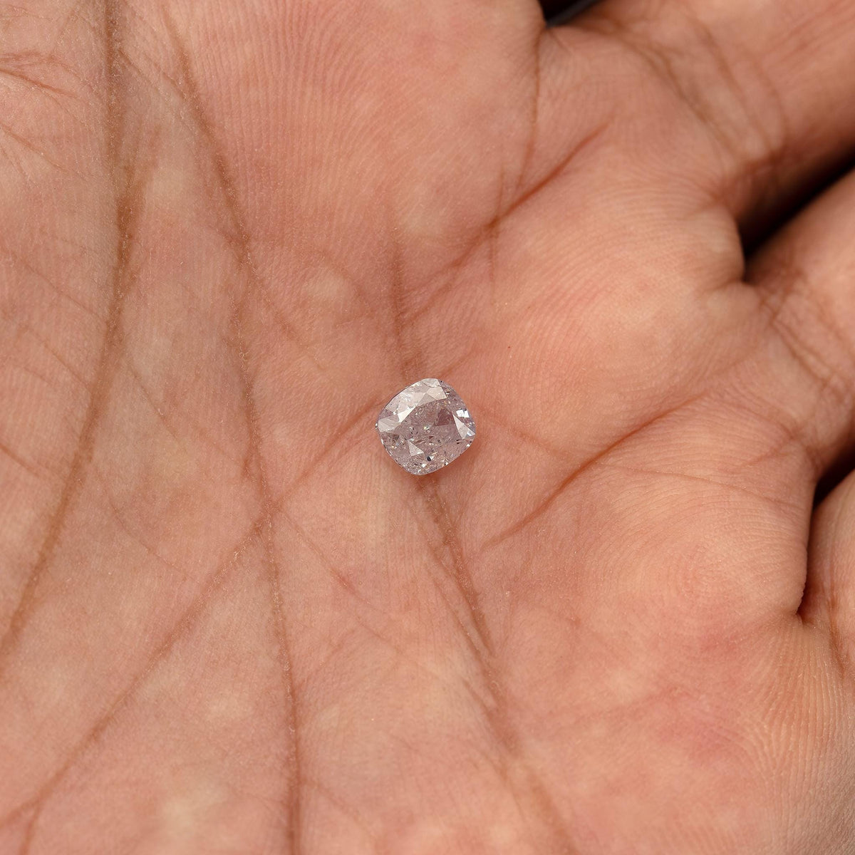 Loose light pink cushion diamond resting in an open palm for relative size.