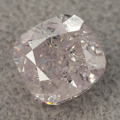 Macro of the natural light pink cushion diamond on a gray surface, showing its facets and visible inclusions.