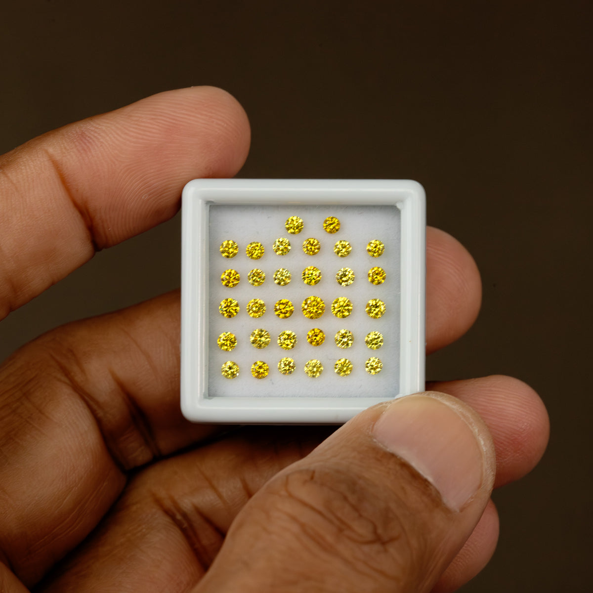 Hand-held white tray of yellow round diamonds, showing the display against fingers for scale.