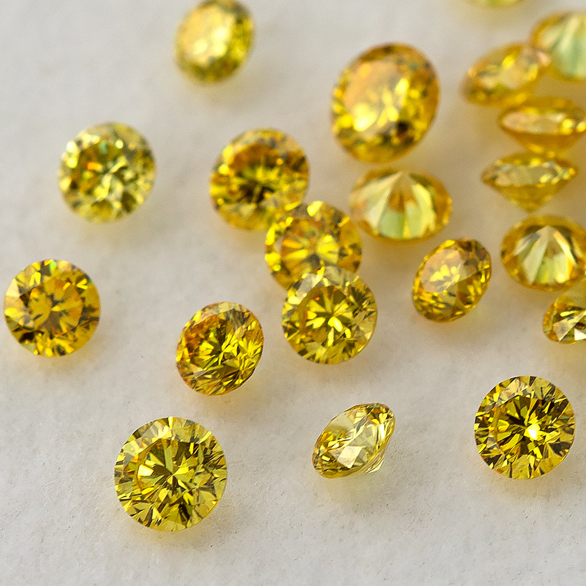 Close mixed-angle cluster of yellow diamonds on a white surface, showing face-up and side facets.