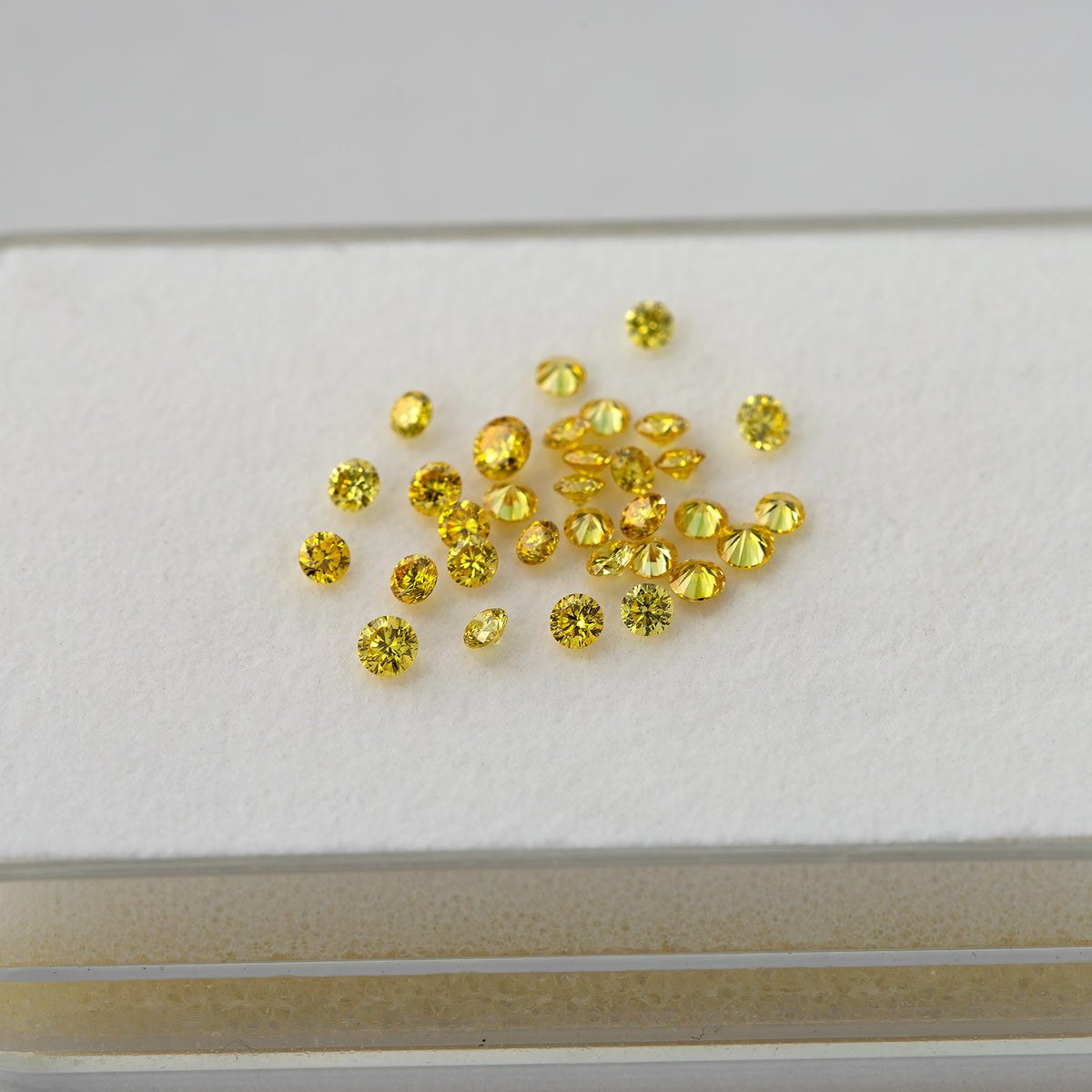 Wider view of loose yellow diamonds scattered on a white grooved surface.