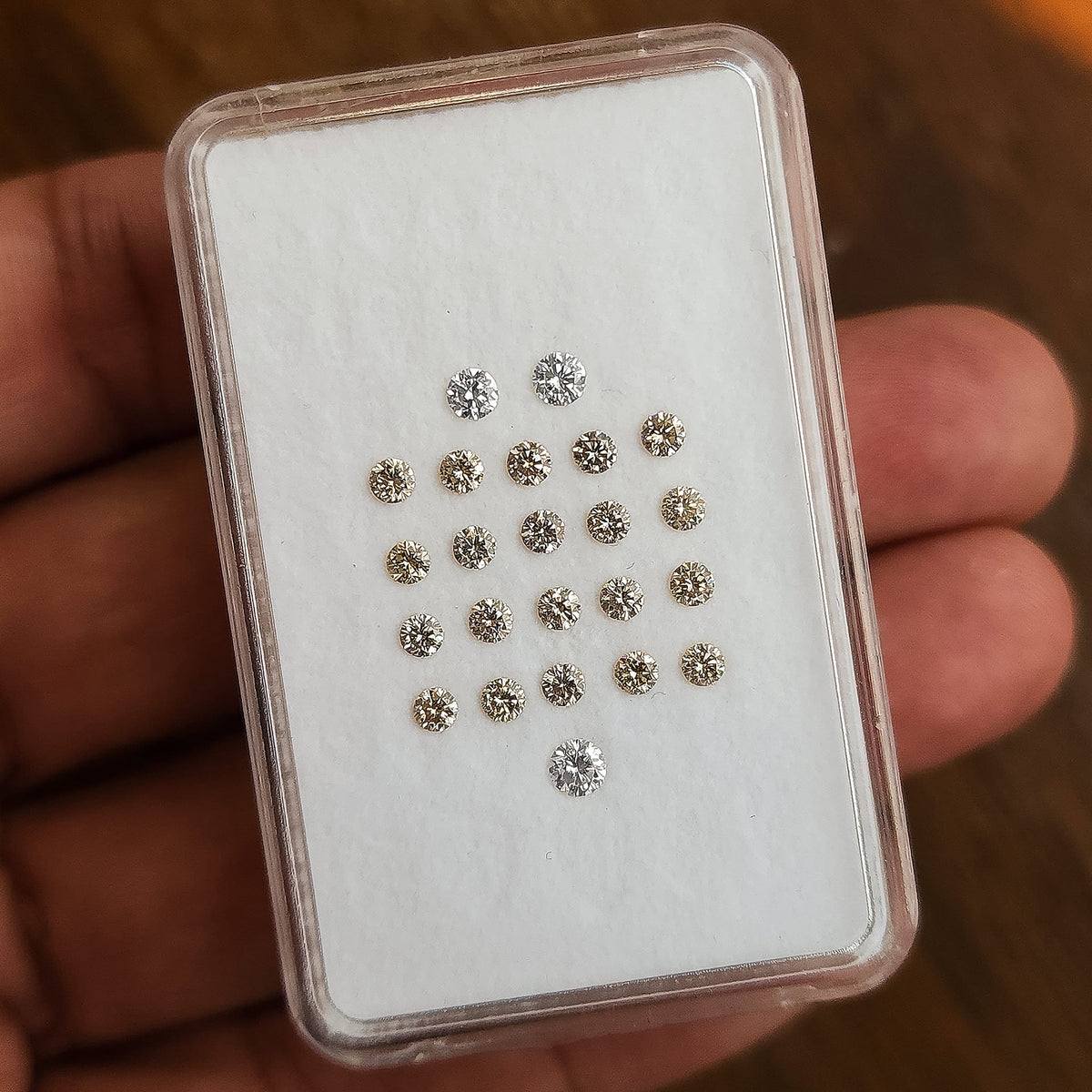 Parcel box of representative 2.5mm champagne round diamonds held in hand for scale.