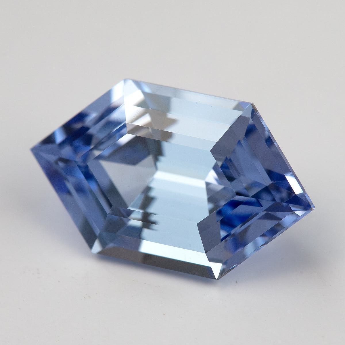 Angled view of a cornflower-blue lab-grown sapphire on a pale surface, showing bright central facets and blue edges.