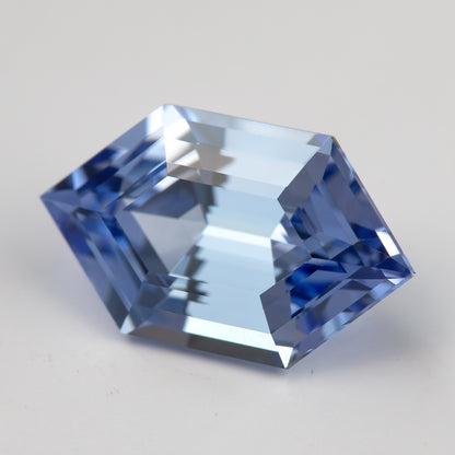 Angled view of a cornflower-blue lab-grown sapphire on a pale surface, showing bright central facets and blue edges.