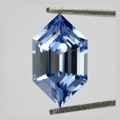 Cornflower-blue lab-grown sapphire held upright between tweezers, with light and dark blue facet reflections.