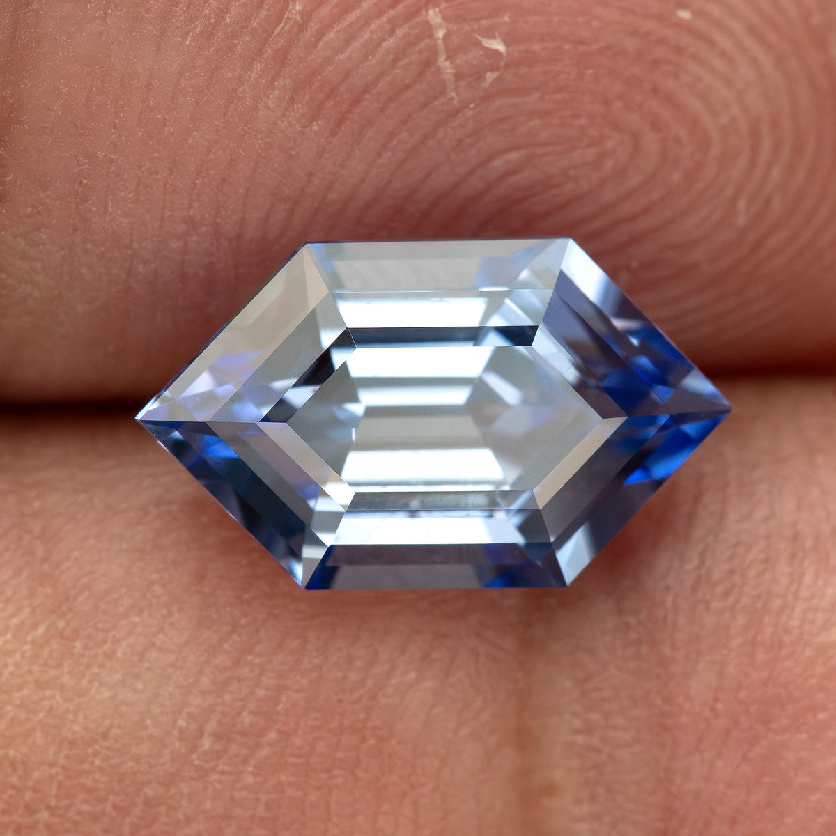 Cornflower-blue lab-grown sapphire resting horizontally against fingers, showing its elongated hexagonal outline.