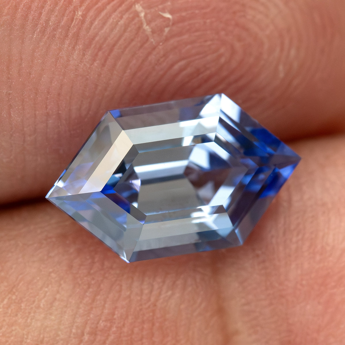 Tilted cornflower-blue lab-grown sapphire against fingers, with bright central facets and blue ends.