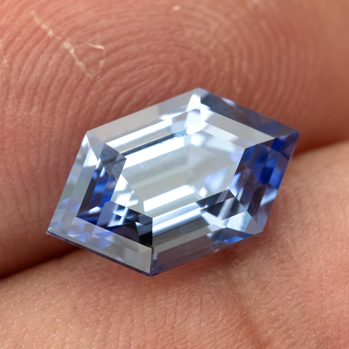 Cornflower-blue lab-grown sapphire against fingers, with pale central reflections and blue edge facets.