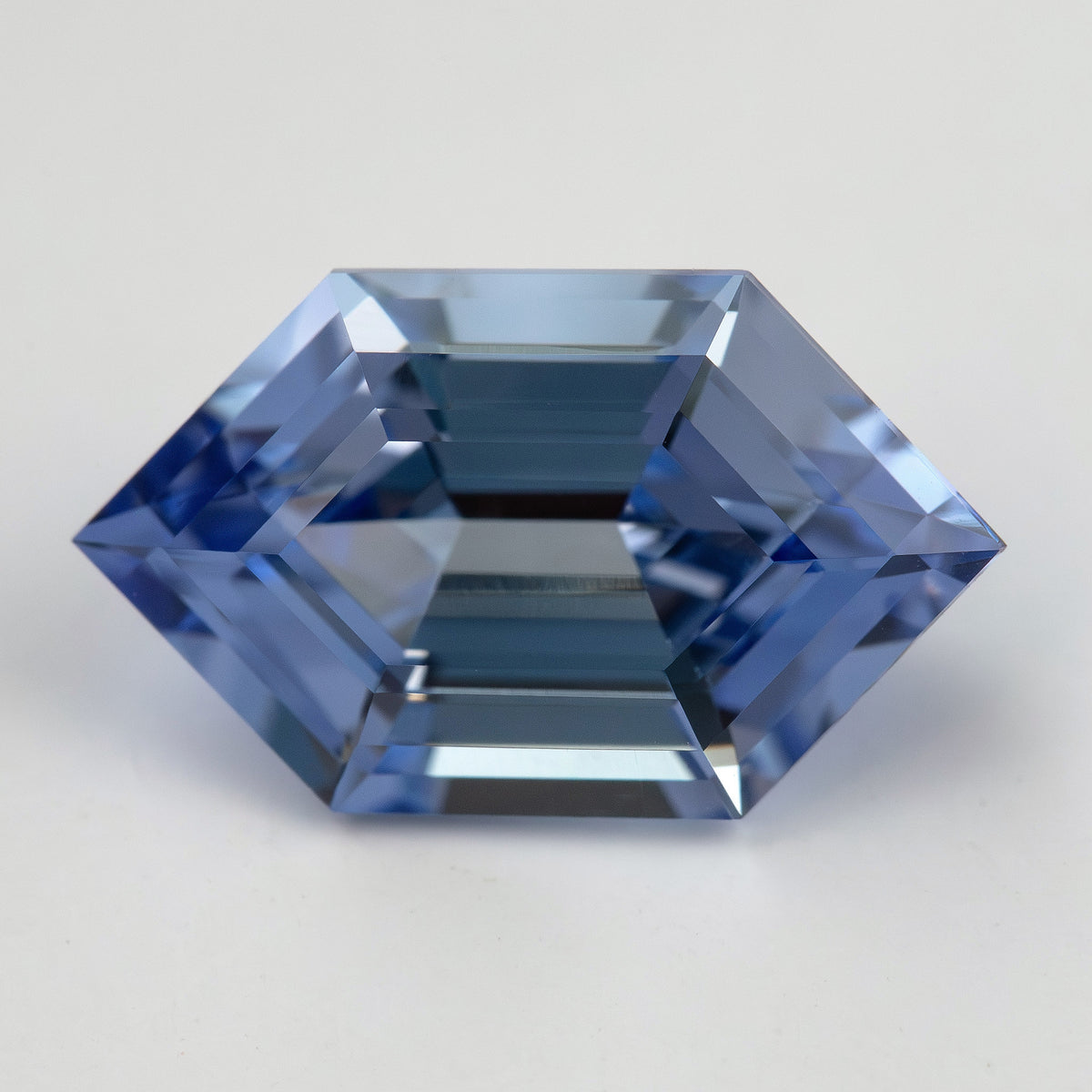 Horizontal face-up view of a cornflower-blue lab-grown sapphire on a pale surface, showing its step-facet pattern.