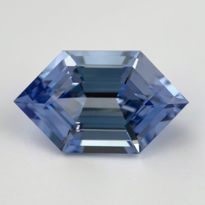 Horizontal face-up view of a cornflower-blue lab-grown sapphire on a pale surface, showing its step-facet pattern.