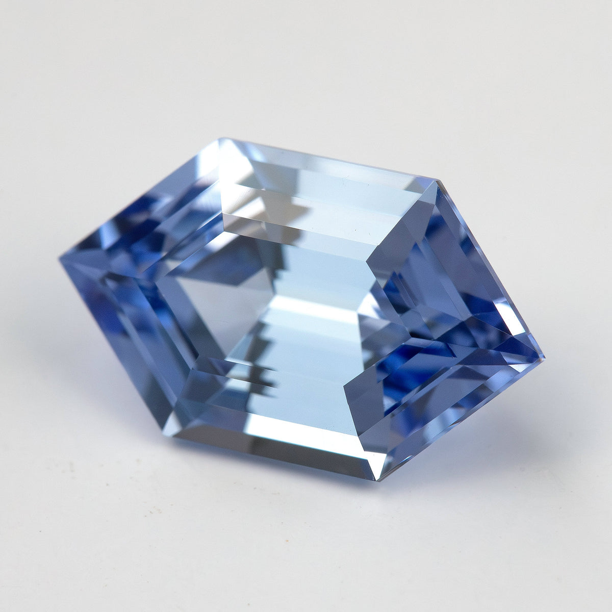 Angled cornflower-blue lab-grown sapphire on a pale background, with bright white and blue facet reflections.