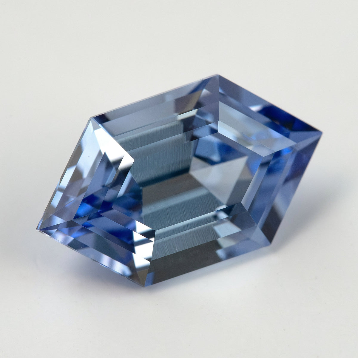 Three-quarter view of a cornflower-blue lab-grown sapphire on a pale surface, showing its raised profile and facets.