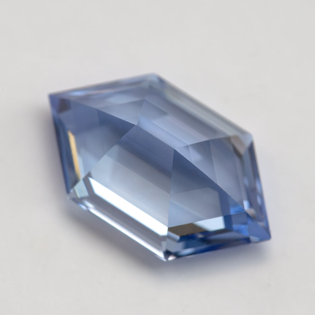 Low angled view of a cornflower-blue lab-grown sapphire on a pale surface, showing its profile and broad pale facets.