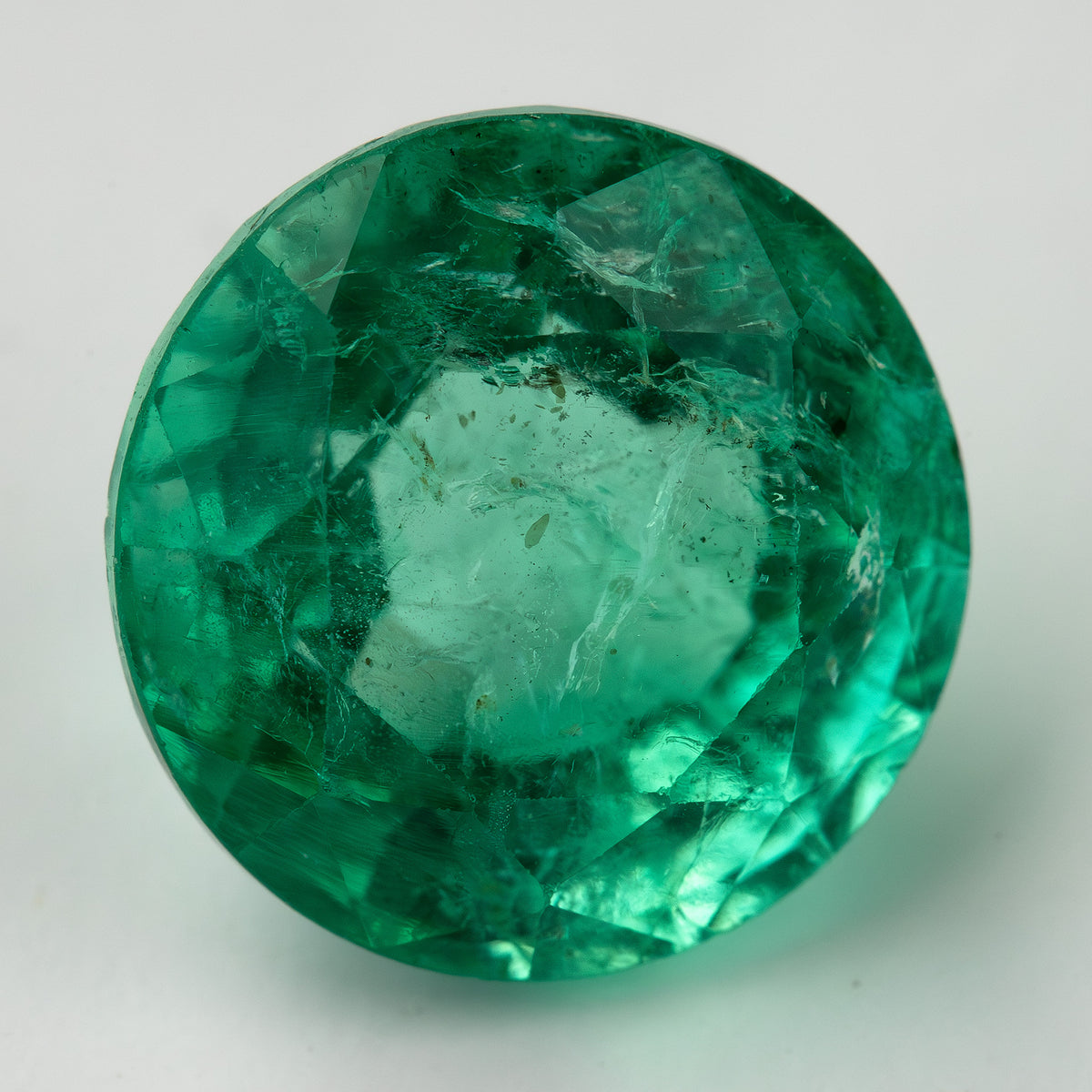 Second face-up macro of the round green emerald on white, with a lighter center and darker green edge facets.