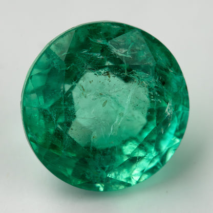 Second face-up macro of the round green emerald on white, with a lighter center and darker green edge facets.