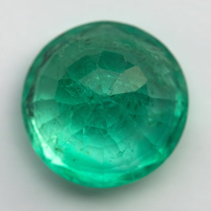 Reverse view of the round green emerald on white, showing pavilion facets meeting near the center.