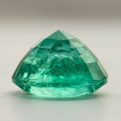 Side profile of the round green emerald on white, showing crown and pavilion depth.