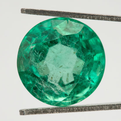 Face-up tweezer view of the round green emerald on white, showing the full circular outline.