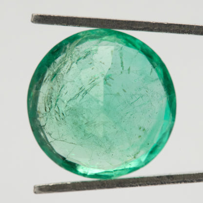 Close face-up view of the round green emerald in tweezers, showing the broad central table and internal features.