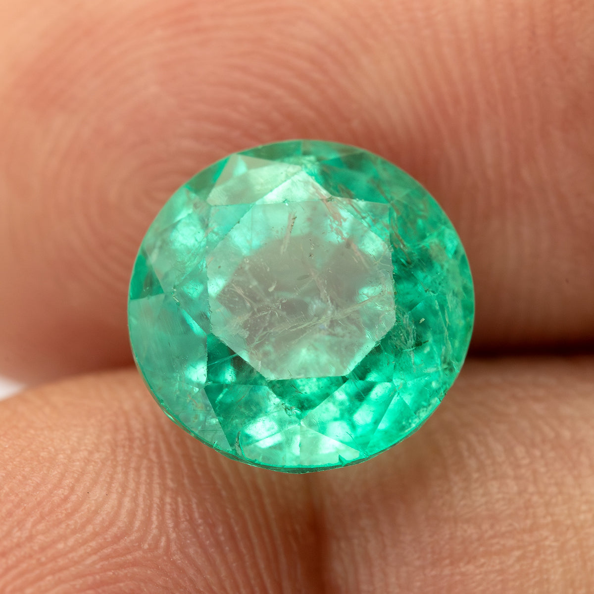 Round green emerald supported on fingertips, showing the face and circular outline from a slight angle.