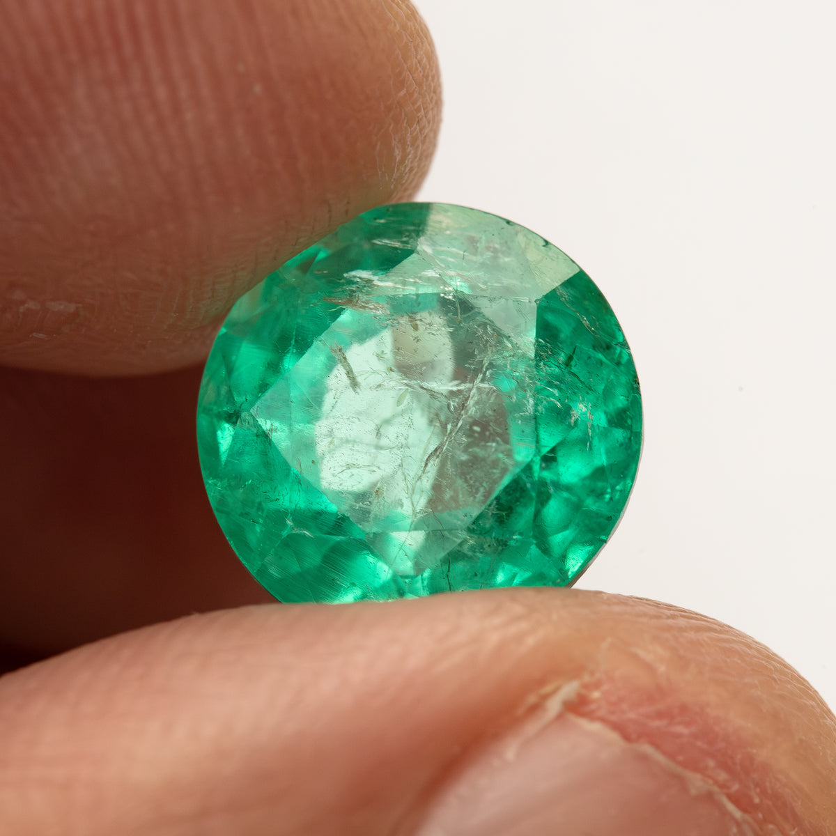 Second fingertip-supported view of the round green emerald with a different central reflection.