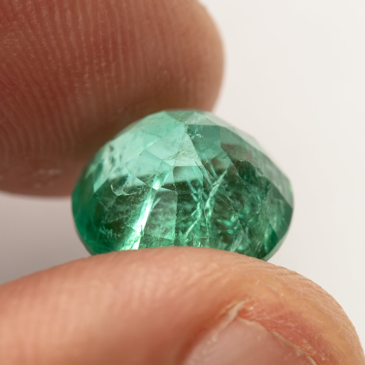 Angled fingertip profile of the round green emerald, showing the pavilion and lower edge.