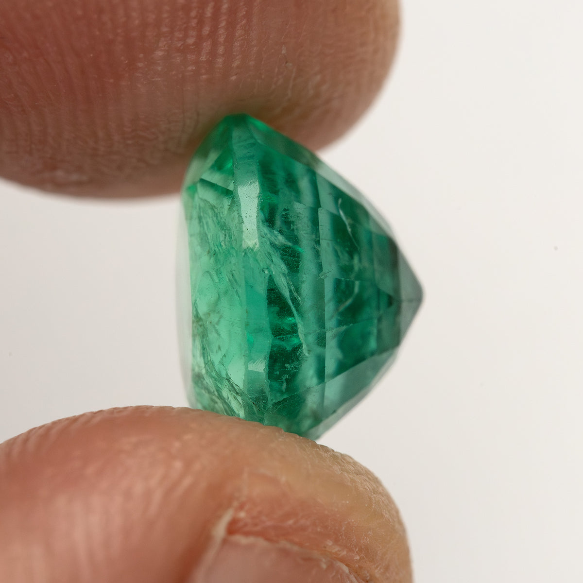Near-profile fingertip view of the round green emerald, showing its depth from the side.