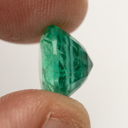 Near-profile fingertip view of the round green emerald, showing its depth from the side.