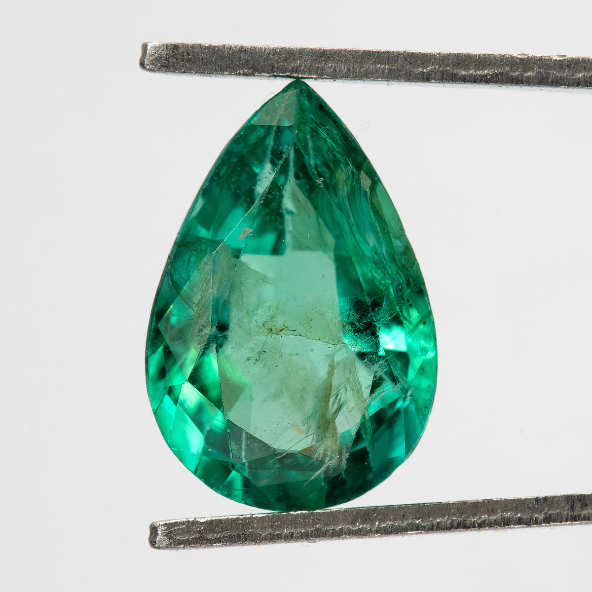 Pear emerald held face-up point-up in tweezers, with table facets and visible jardin.