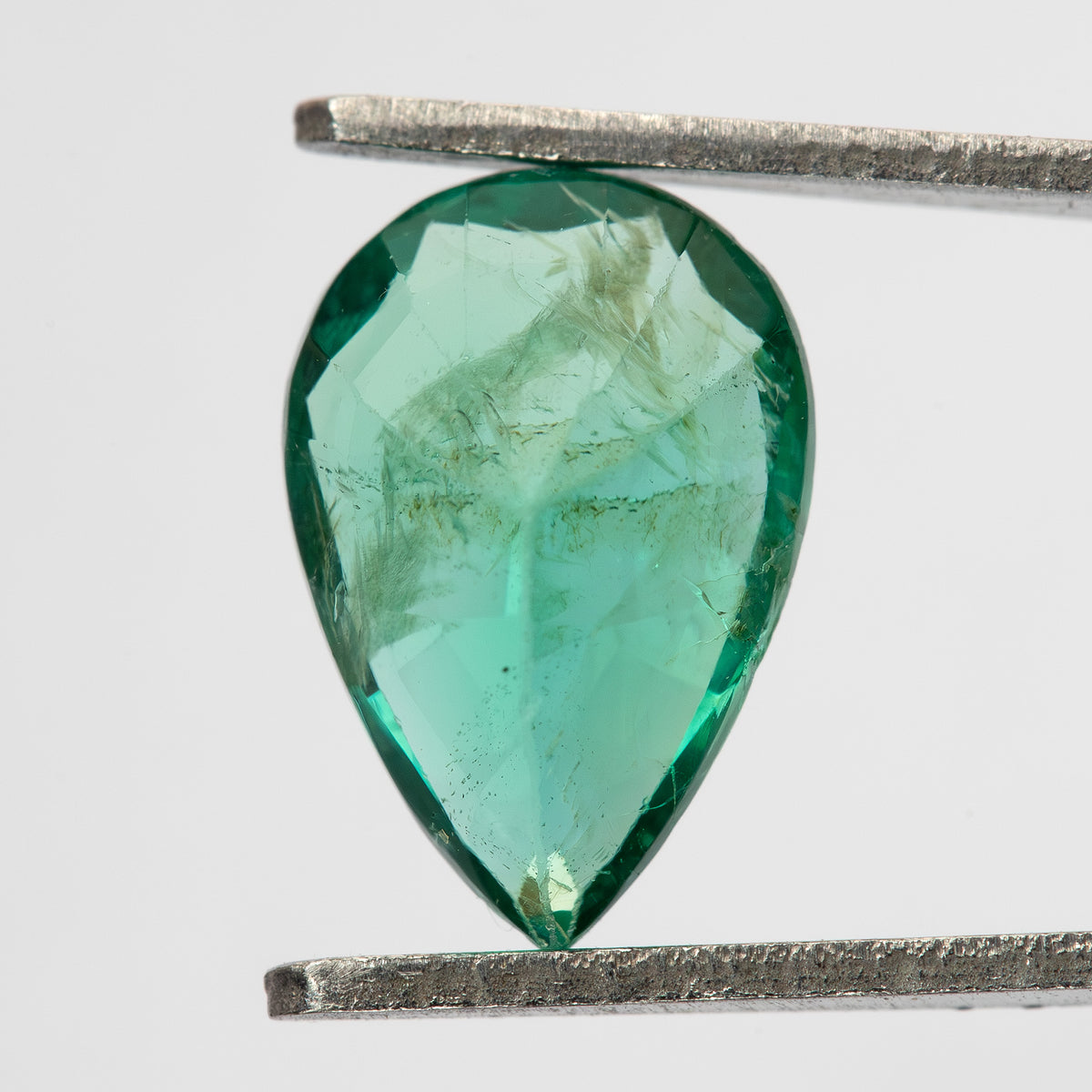 Reverse view of pear emerald in tweezers, showing pavilion facets and visible internal features.