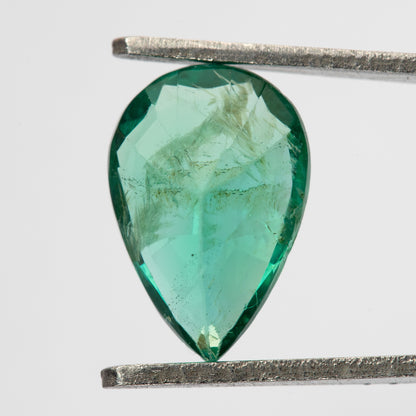 Reverse view of pear emerald in tweezers, showing pavilion facets and visible internal features.