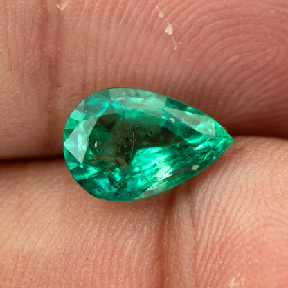 Green pear emerald resting face-up between fingertips, showing its outline and size.