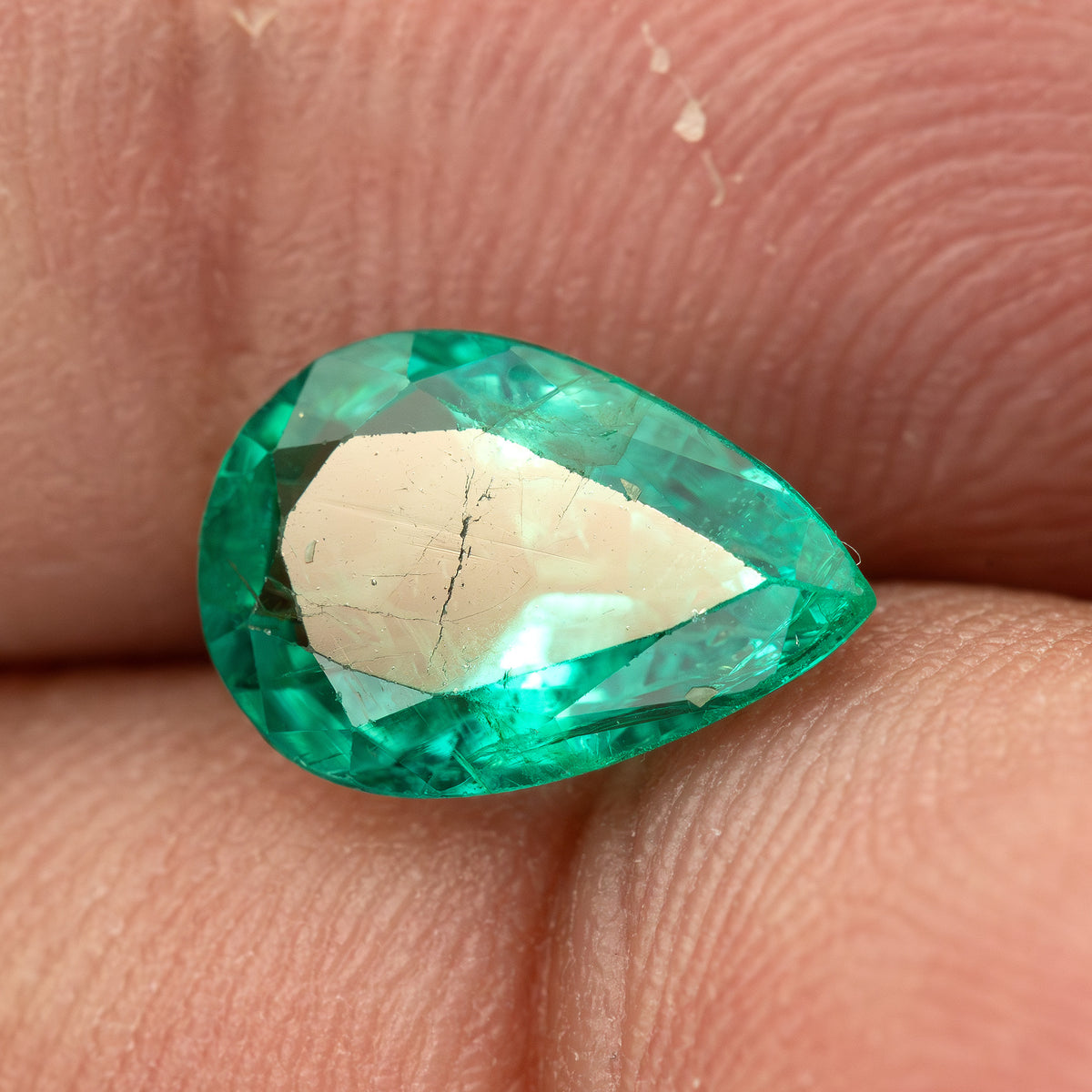 Pear emerald between fingertips with a bright reflection across the central table.