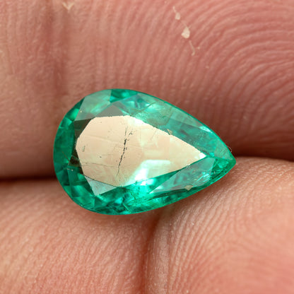 Pear emerald between fingertips with a bright reflection across the central table.