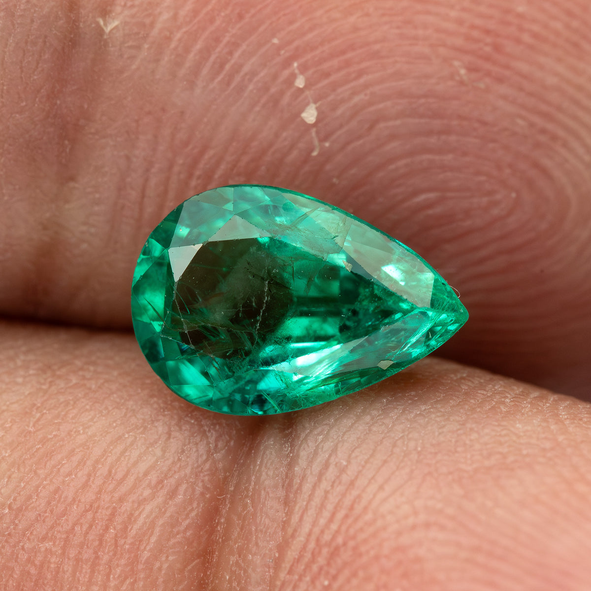 Face-up pear emerald resting horizontally against fingertips.