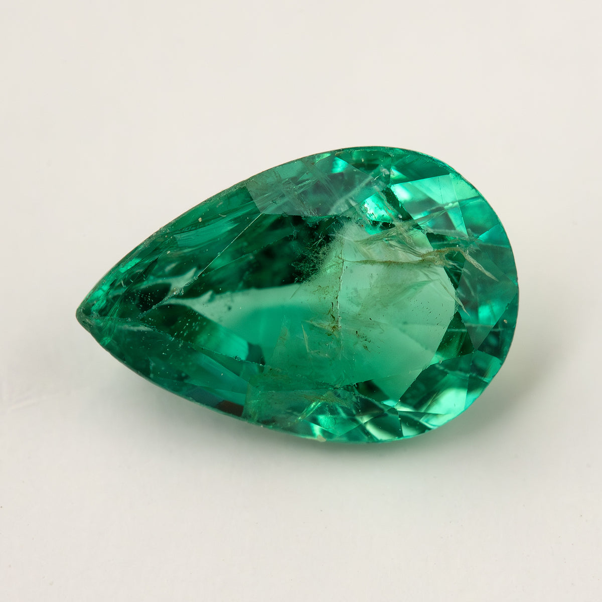 Green pear emerald lying face-up on a pale surface, with its table and visible jardin.