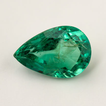 Green pear emerald lying face-up on a pale surface, with its table and visible jardin.