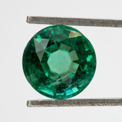 Face-up tweezer view of the round green emerald on white, showing a different central reflection.