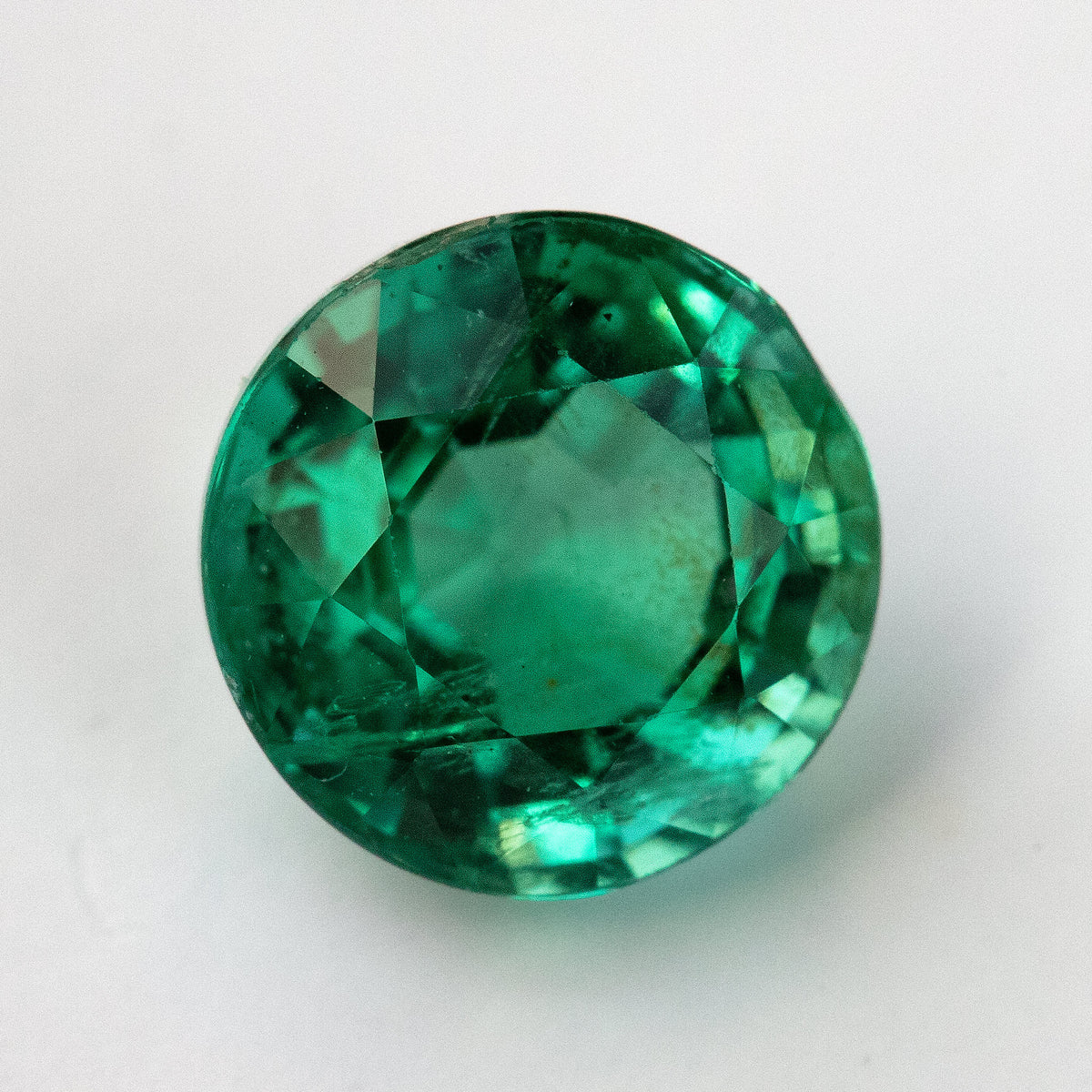 Face-up loose view of the round green emerald on white, showing the table and lower internal features.