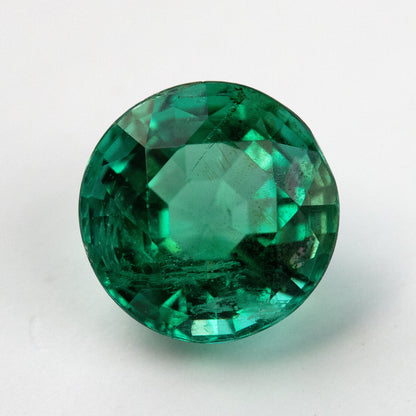 Second loose face-up view of the round green emerald on white with a darker central reflection.